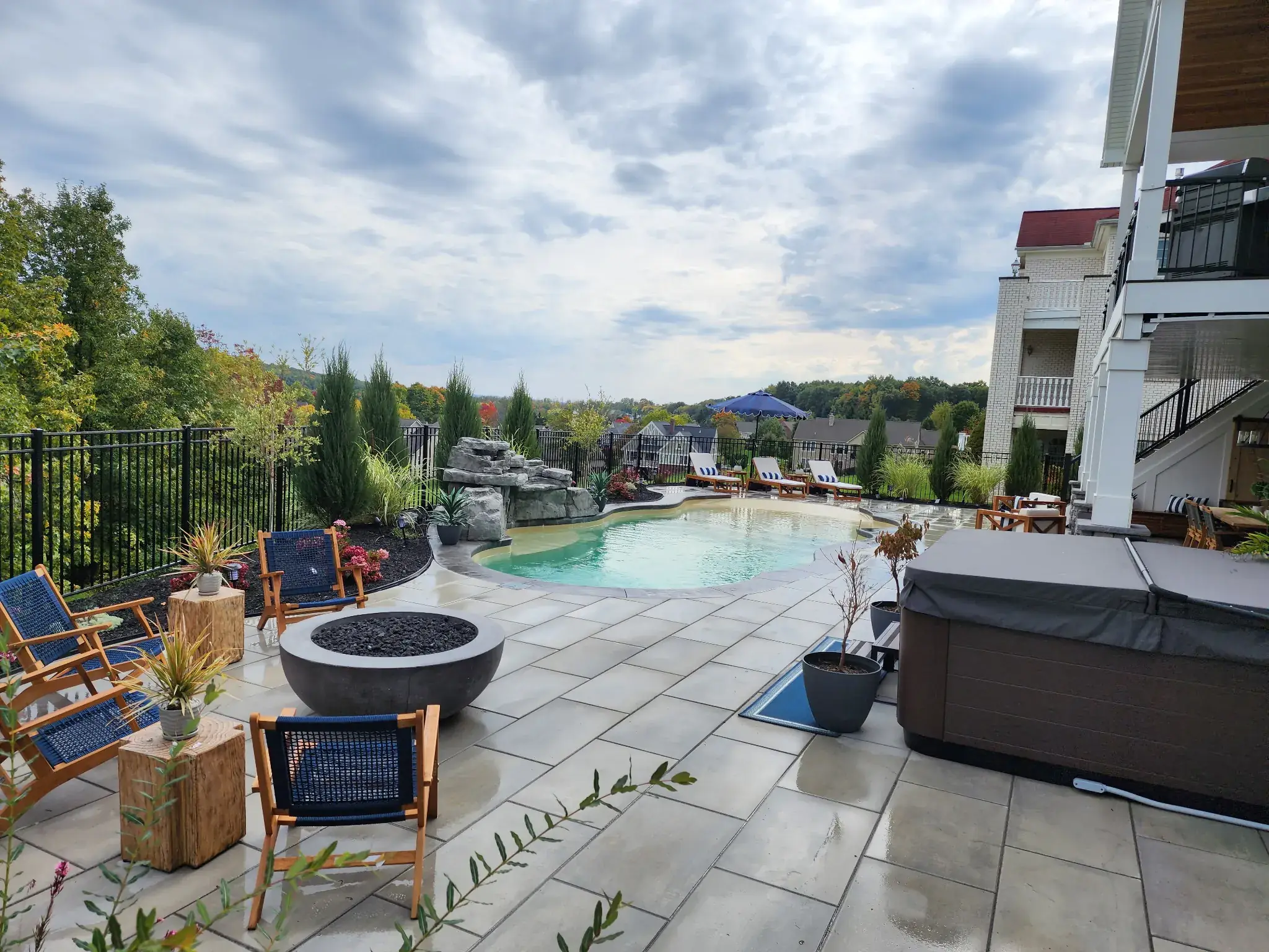 Paver patio with a fire bowl and seating area beside a pool with a rock waterfall