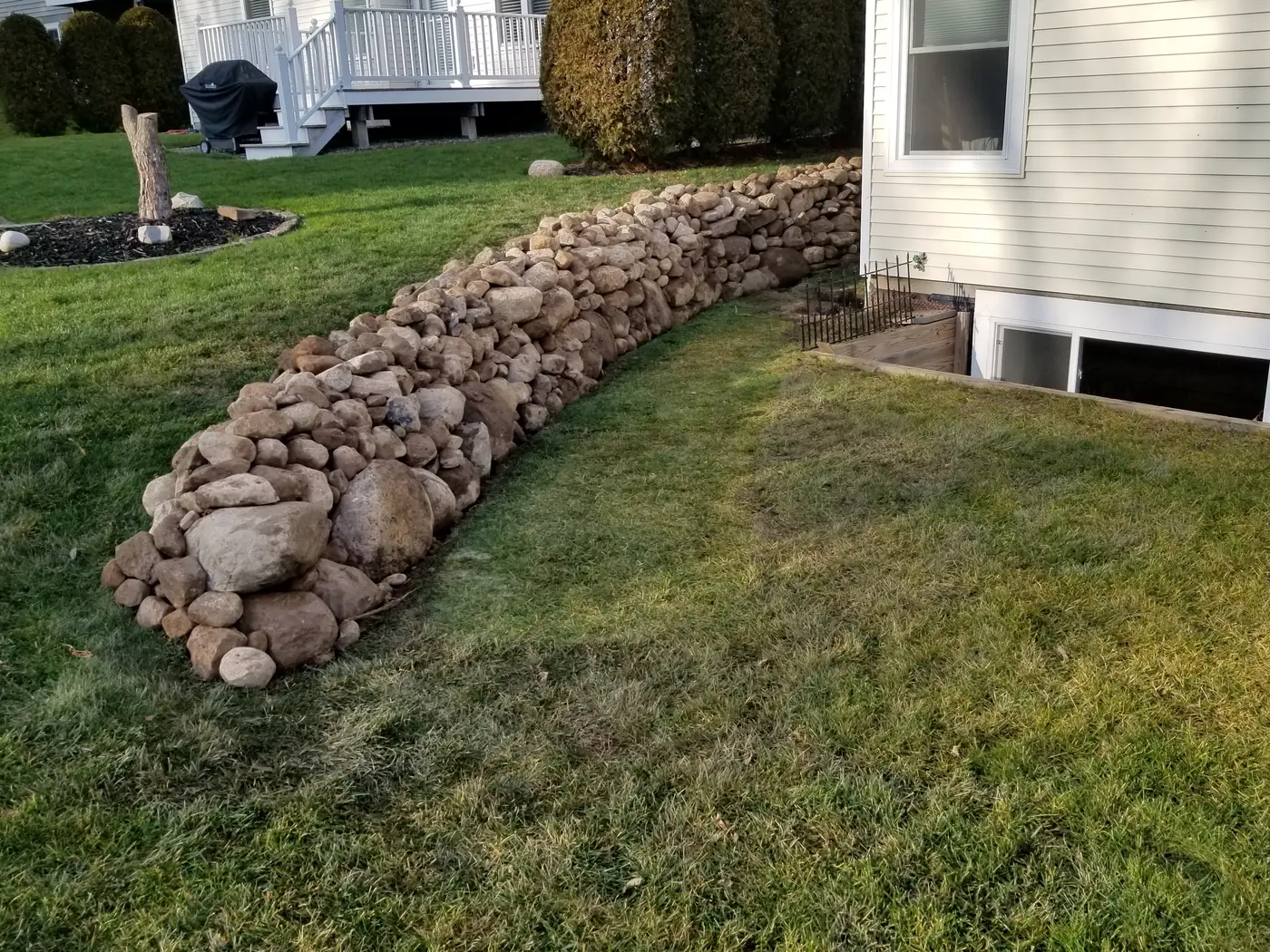 Boulder wall along the side of a house with a fresh lawn