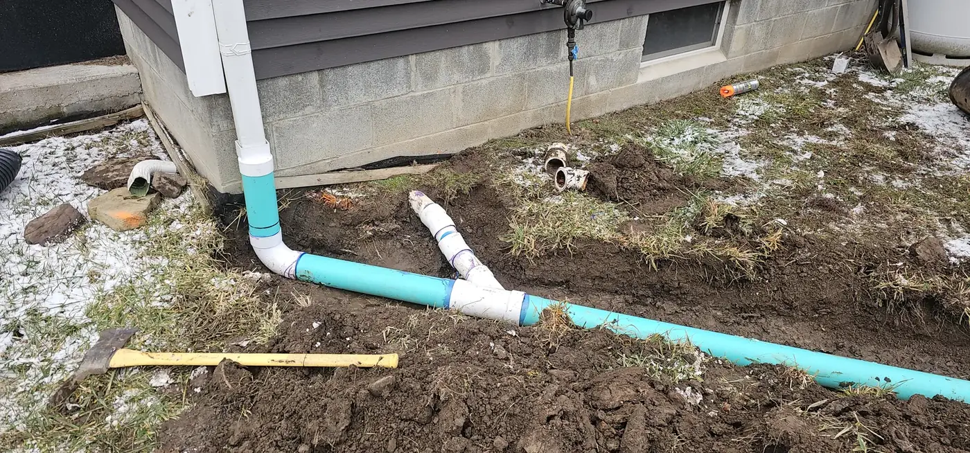 Downspout connected to an underground drain pipe beside a foundation