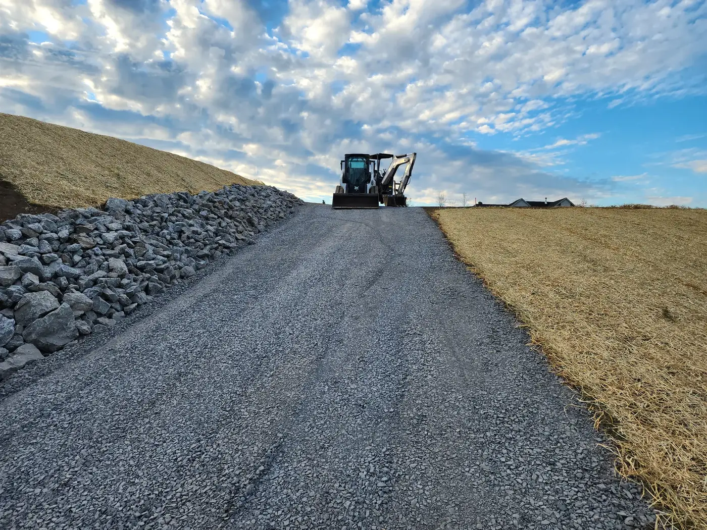 Freshly graded gravel driveway with an excavator at the far end