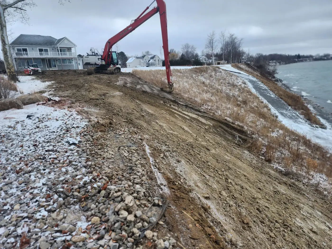 Long reach excavator leveling a sloped bank beside a lake