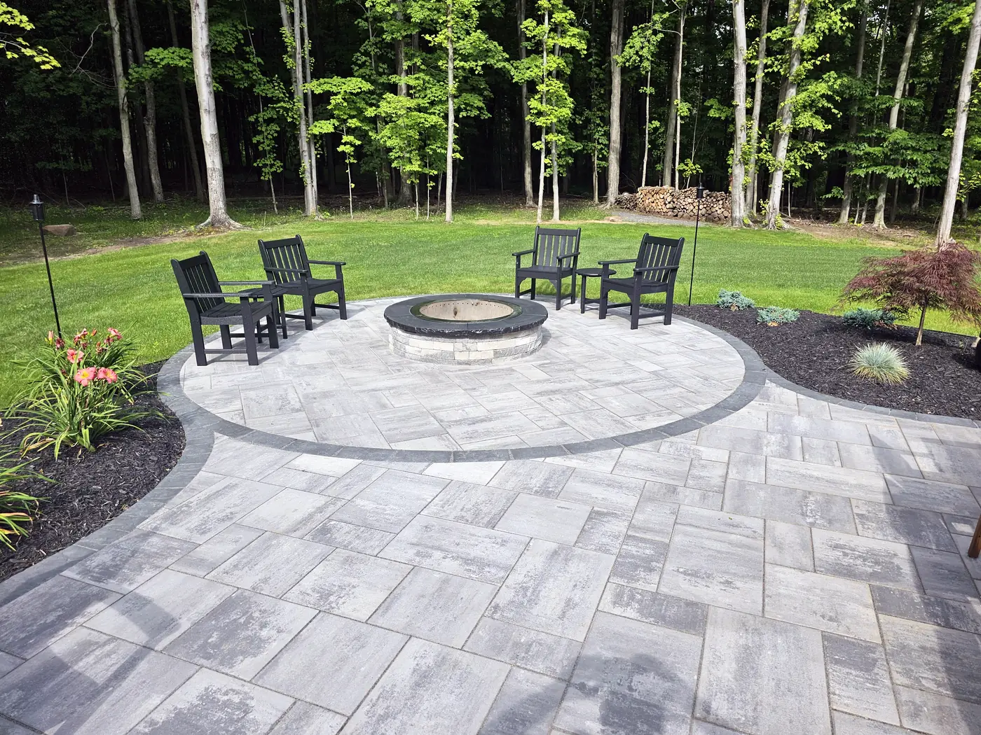Round paver patio with a fire pit, Adirondack chairs and plantings