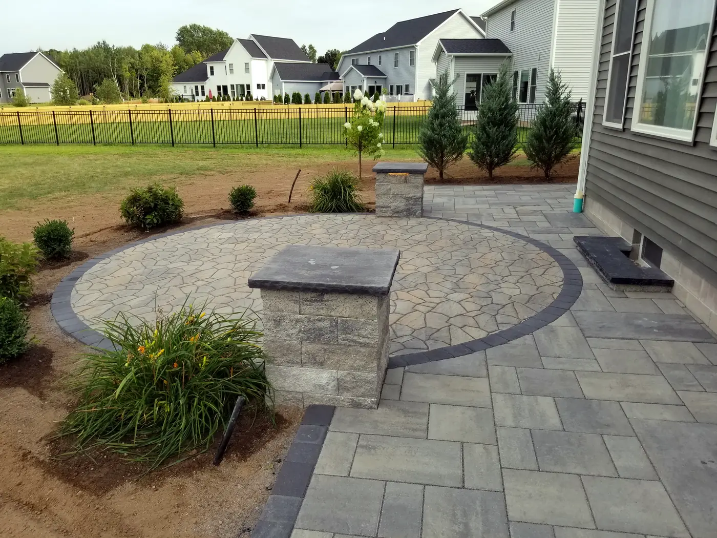 Round flagstone style paver patio with stone pillars and new plantings