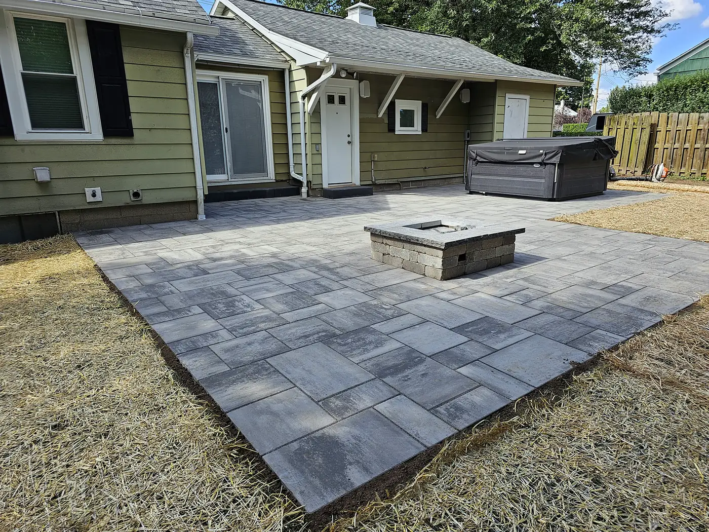 Rectangular paver patio with a fire table behind a green house