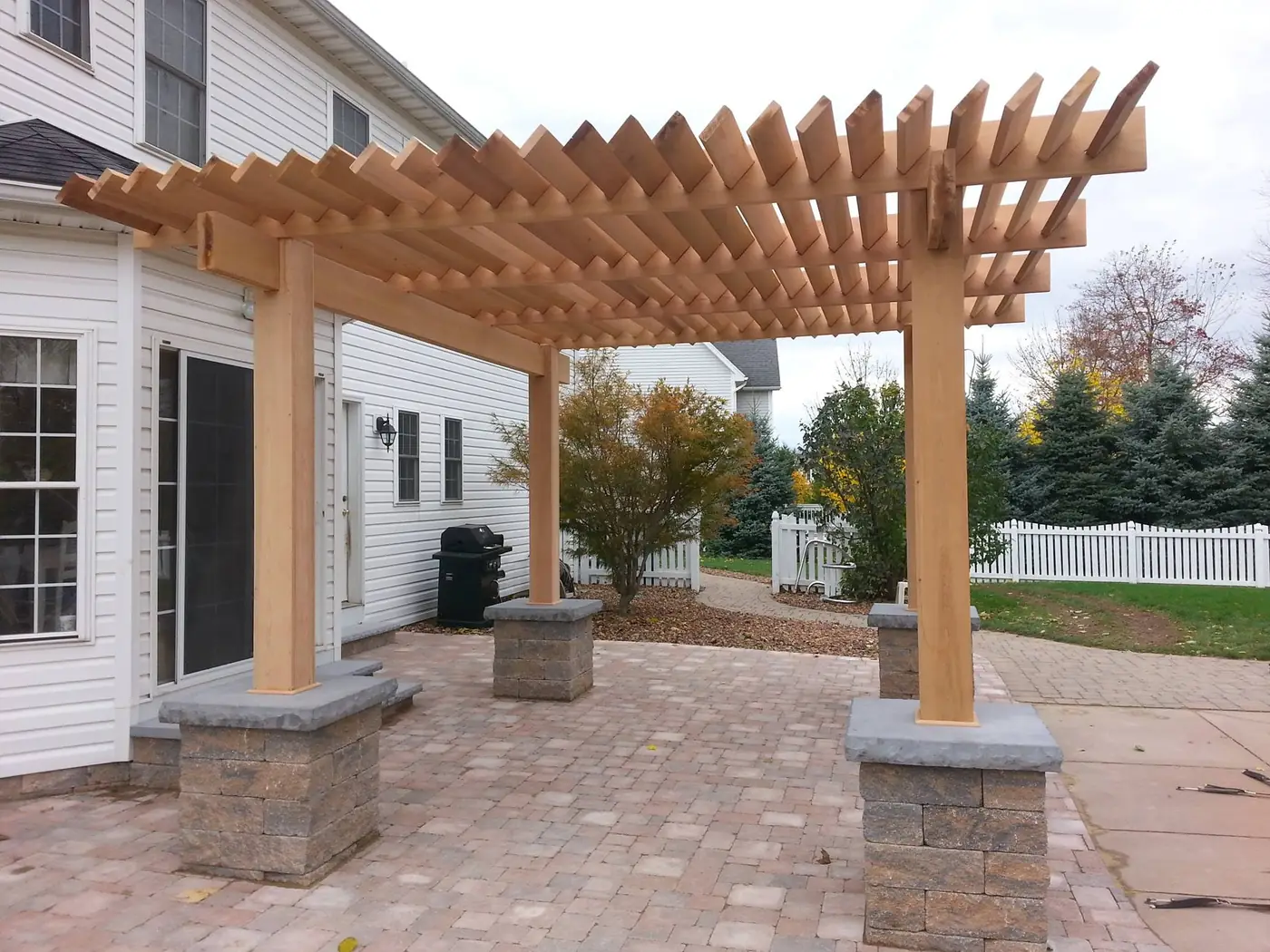 Paver patio with stone pillars under a cedar pergola