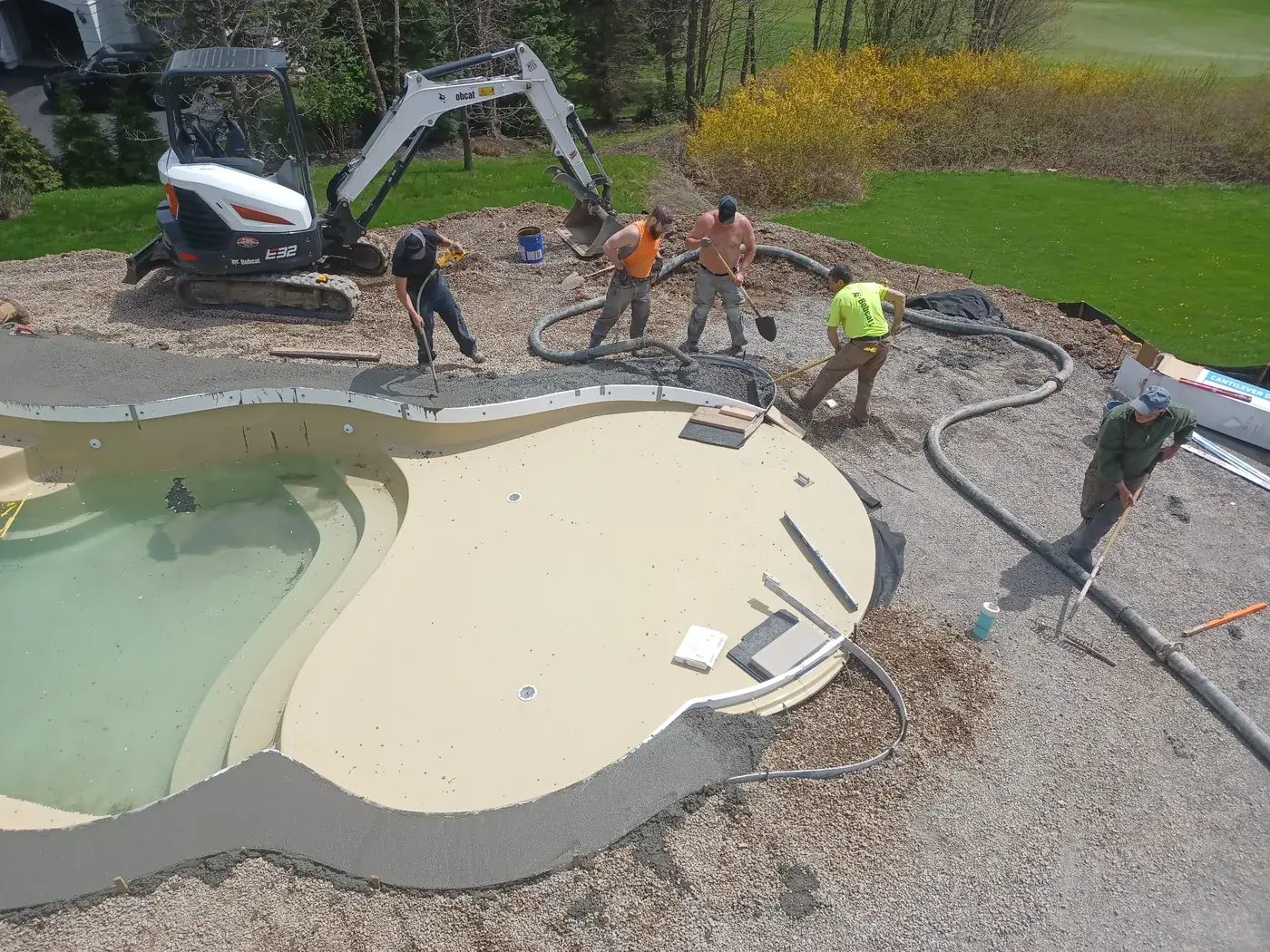 Crew working around a newly set pool with a mini excavator during construction