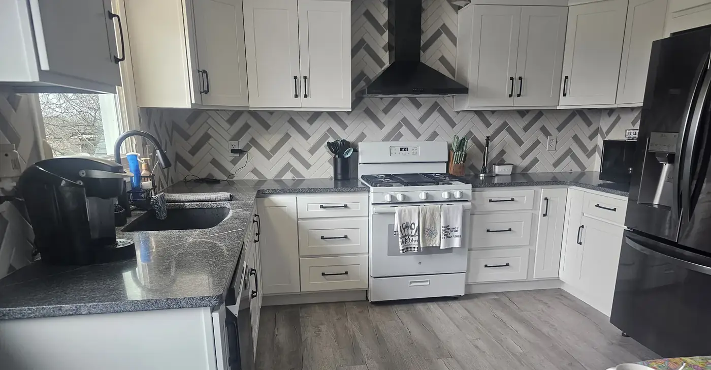 Remodeled kitchen with white cabinets and a herringbone tile backsplash