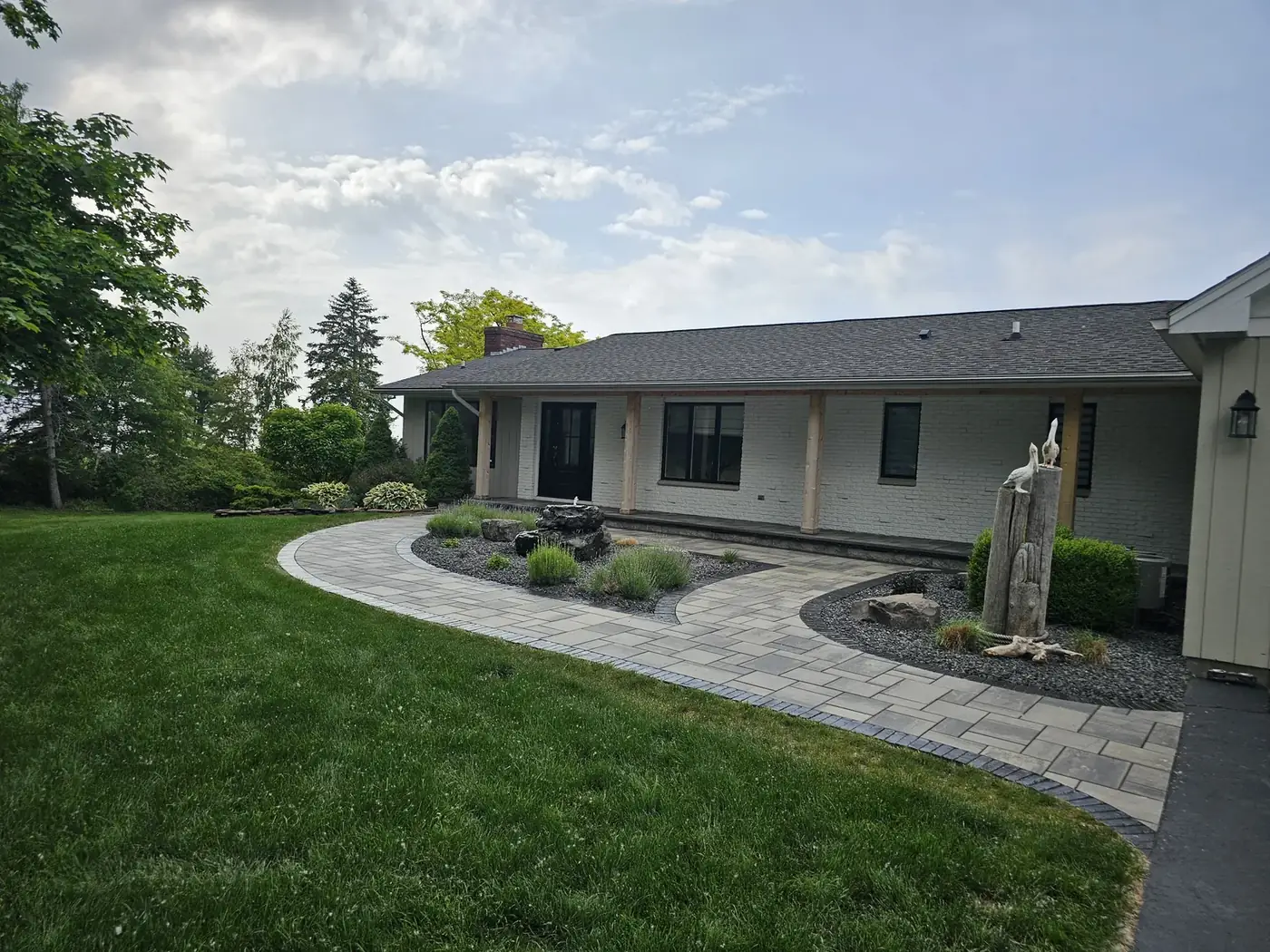 Curved paver walkway leading to the front of a ranch home with landscape beds